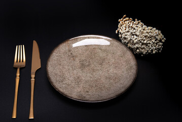 Table set in detail, with napkin, beautiful plate and beautiful cutlery, on a dark surface with small flowers, selective focus.