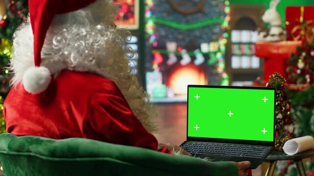 Santa Claus making list of kids who has been naughty or nice on green screen laptop. Person preparing travel plans on chroma key notebook before visiting children, camera A