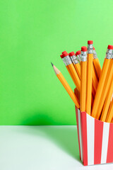 Graphite orange pencils in red-white box for french fries close on the green wall. Back to school