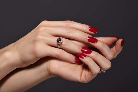 Close up of female hands with red gel polish manicure on nails and luxury rings. Timeless elegance for beauty salons, nail masters, and advertising of professional nail care and hand treatment