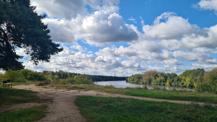 A serene landscape featuring a river surrounded by lush greenery and trees under a blue sky with fluffy clouds. Ideal for nature concepts and copy space.