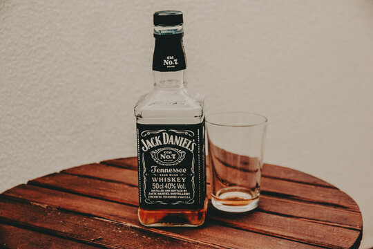 Kyiv, Ukraine 7 May 2024 Jack Daniel's whiskey with and empty glass on a wooden table Tennessee whiskey sitting on a rustic, dark wooden round table. The background is a plain, off-white wall.