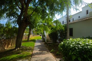 Sunny garden pathway with trees, stone walls, and traditional white houses, creating a peaceful Mediterranean atmosphere in a residential area. Albufeira. Portugal