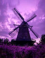 A majestic windmill stands tall against a dramatic purple sunset sky, framed by a field of vibrant purple wildflowers.