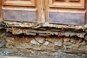 Crumbling masonry foundation with plaster decay brick erosion and soil exposure at the entrance door of old historic building. Urgent repair maintenance and construction restoration