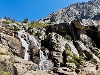 A stunning waterfall cascades down massive granite cliffs under a bright blue sky