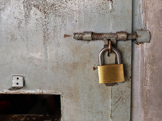  A close-up view of a large, shiny golden padlock, securely fastened on a heavy, old, and rusty prison door. The contrast between the bright, new-looking lock and the decaying, weathered door surface 