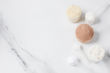 Assorted protein powder and supplement scoops on white marble background for nutrition and fitness