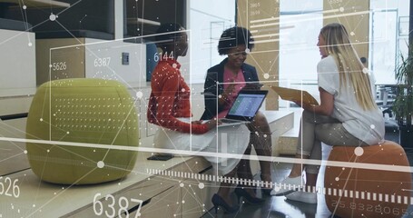 Collaborating three coworker women using laptop, tablet and holding yellow folder in office lounge