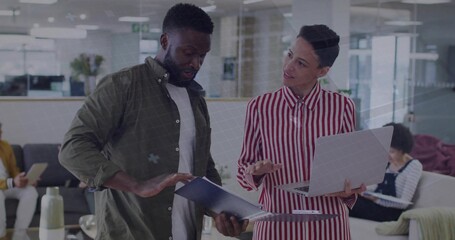 Reviewing blue document folder, two colleagues collaborating over silver laptop in office lounge