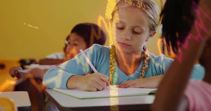 Schoolgirl wearing light blue top writing in notebook at school desk, with pencils