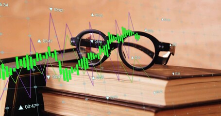 Resting black round eyeglasses atop hardcover books on office desk, displaying stock market graphs