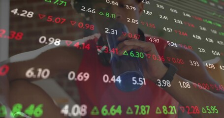 Drinking man wearing black watch sipping from blue shaker bottle in gym, with stock ticker overlay