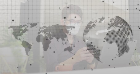 Analyzing data on smartphone by Asian man at desk with laptop, mug, plant, world map overlay