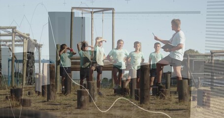Children in green uniforms balancing on obstacle course stumps while coach pointing clipboard