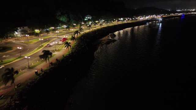 Drone flies along Avenida Amador at night, with streetlights and moving traffic, dark waters on both sides, heading toward Perico and Flamenco Islands in Panama