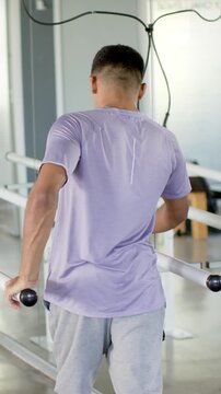 Male patient gripping parallel bars undergoing therapy in rehab gym, with harness and mirror