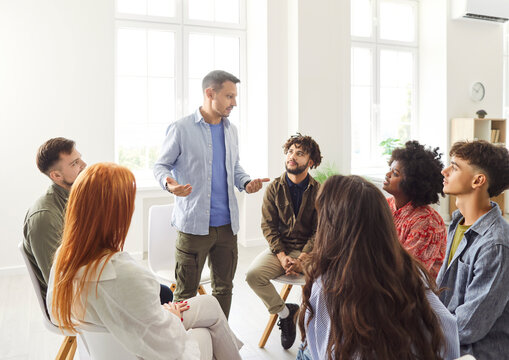 Male speaker at psychologist meeting patients at group therapy, team counselor giving advices to diverse employees, confident business coach speaking training staff at office, addiction treatment