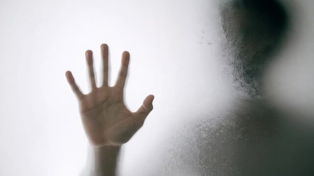 Blurred figure and hand behind frosted glass