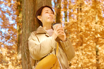 紅葉の中をコーヒーを飲む女性　ミドルエイジ