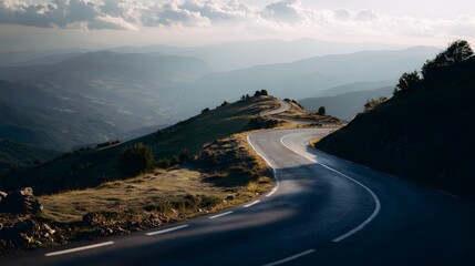 Fototapeta premium Winding mountain road descends through a valley bathed in the golden light of sunset.