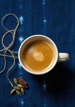 A cup of coffee with cardamoms and twine on blue tie dye fabric from above eye level close up shot