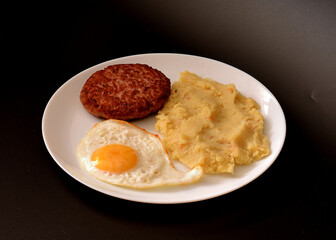 Fried meat cutlet with mashed potatoes and boiled chicken egg in a round plate on a black background.