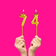 Birthday on a fuchsia background with the number 74 - Hands holding number-shaped candles