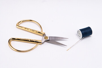 Gold Handled Scissors with Needle and Dark Thread Spool on White Background.