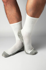 Close-up shot of a man's legs and feet, showing him standing on tiptoe while wearing white ribbed athletic socks with gray heels and toes