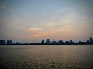 Fototapeta premium Serene Dusk on West Lake, Hanoi – Gentle Peach Sky and Quiet City Waterfront