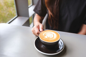 Closeup image of a woman holding a cup of hot latte coffee on the table