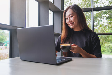 Fototapeta premium Portrait image of a woman working on laptop computer while drinking coffee in cafe