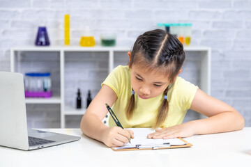 A smiling girl uses a laptop in a science classroom filled with beakers and tubes. Her confidence and cheerful energy reflect how technology supports her learning experience, learning, back to school.