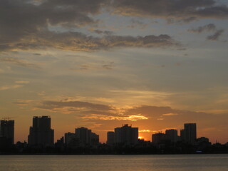 Fototapeta premium Golden Sunset Over Urban Waterfront — Skyline Silhouette and Mirror-Calm Water over West Lake in Hanoi, Vietnam