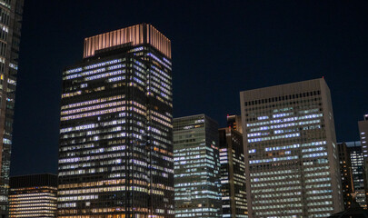 Vibrant cityscape of modern high-rise office buildings glowing with interior lights against dark night sky, dynamic energy of an urban business district.