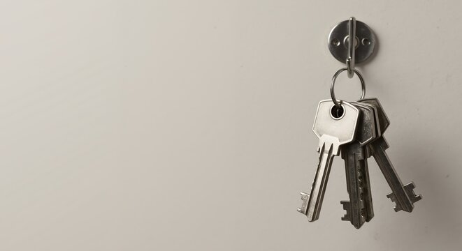 A bunch of keys hanging on a hook against a plain wall. Home security and real estate concept. Minimalist background with copy space for text.