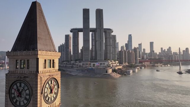 Aerial drone tracking revealing landmark clock tower beside riverfront, highlighting contemporary urban design of raffles city complex against chongqing skyline