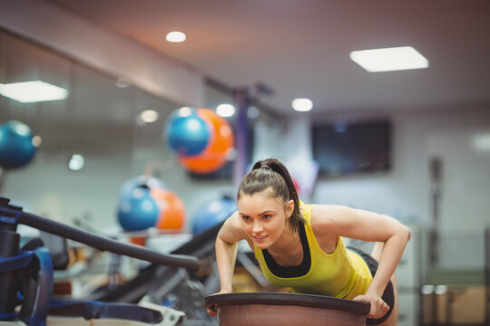 Woman in twenties leaning forward on balance trainer at gym wearing yellow top with black leggings
