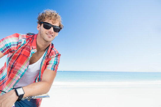 Man leaning on bicycle handlebars on beach wearing sunglasses and smartwatch, copy space