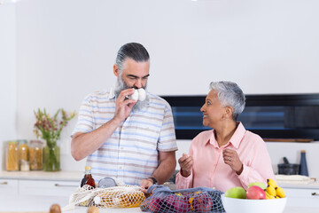 Diverse senior couple unpacking groceries behind kitchen island with mesh produce bags
