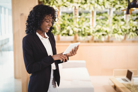 Businesswoman standing in corporate lounge with laptop on table and lush plant wall