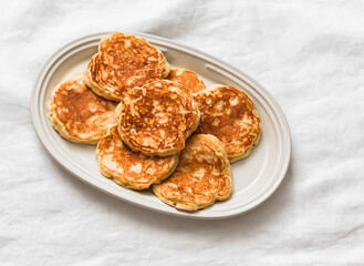 Delicious fluffy pancake fritters on an oval plate on a light background, top view