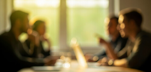 Blurred image of people in a meeting around a table with sunlight glowing through large windows, creating a bright and inspiring atmosphere that suggests collaboration and teamwork.