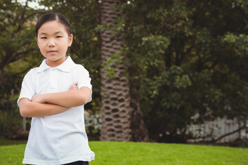 Chinese girl standing with arms crossed on lawn in backyard by palm tree, white picket fence