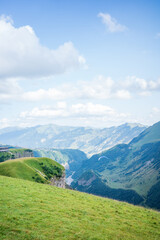 Fototapeta premium Beautiful landscape of a paraglider flying above a lush green valley in the Georgian mountains, with dramatic cliffs, rolling hills, and a river below under a bright blue sky in Kazbegi, Georgia