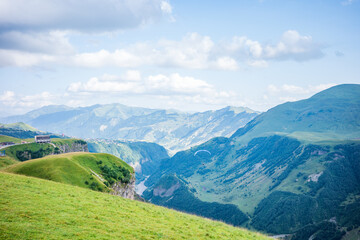Fototapeta premium Breathtaking view of a paraglider soaring above the lush green valleys and dramatic cliffs of the Georgian mountains. A stunning landscape with adventure, freedom, and natural beauty in Kazbegi