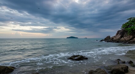 Moody ocean view with rocky shore distant island and cloudy sky