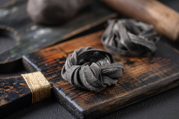 Fototapeta premium Homemade uncooked black tagliatelle noodles on a wooden board