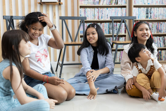 Group of diverse schoolchildren sitting on classroom floor, smiling and talking together. Concept of friendship, teamwork, childhood communication, and social learning in education setting.